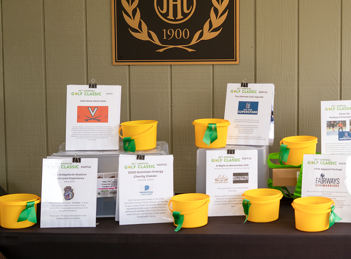 Yellow raffle buckets with green ribbons are displayed on a table in front of raffle prize descriptions at a golf classic—one of the many events for Virginia boys and girls; a dark club emblem with OAC 1900 hangs on the wall behind.