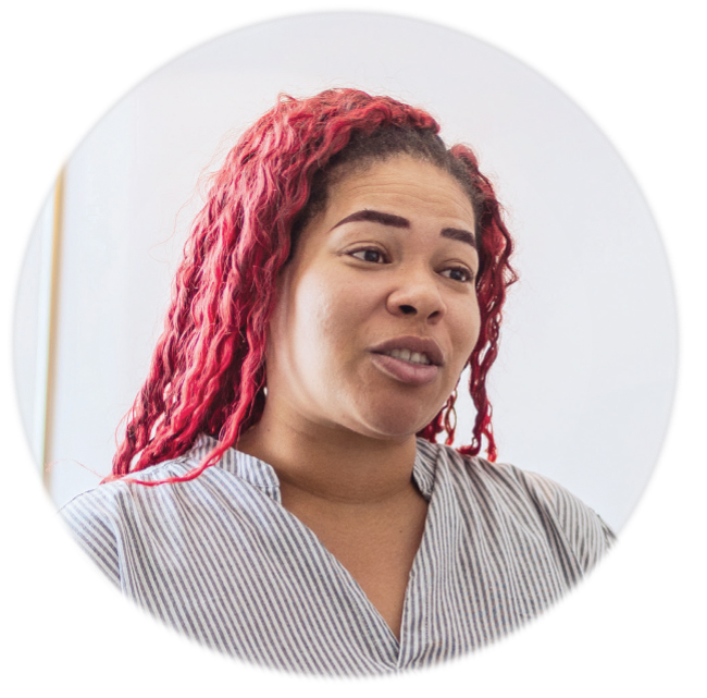A woman with long, bright red hair and a striped shirt is speaking. She appears to be in a well-lit indoor setting, with a neutral, light background.