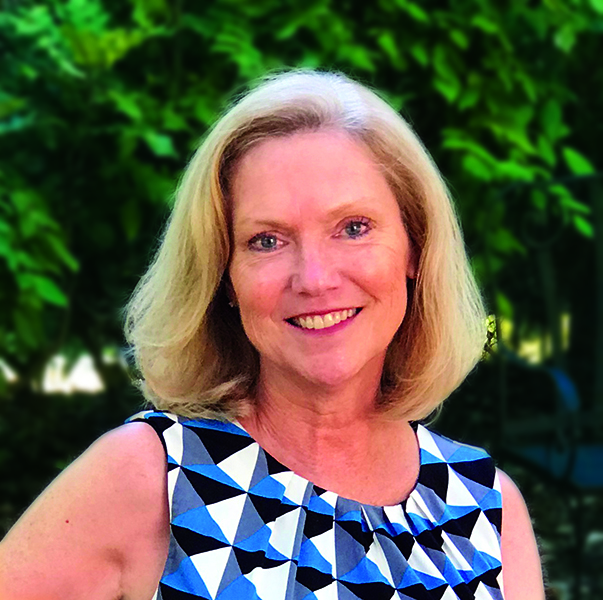 A woman with shoulder-length blonde hair smiles at the camera. She is wearing a sleeveless, geometric-patterned top and standing outdoors with lush green foliage, representing Virginia education and group homes services for boys and girls.